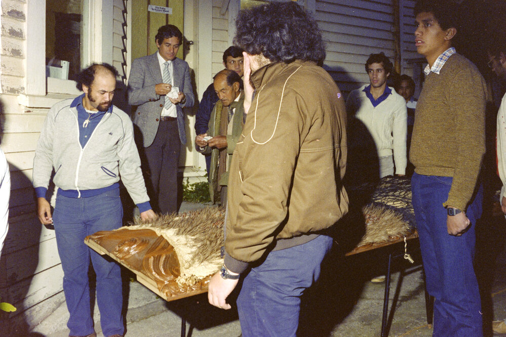 People waiting outside with the carved poupou Taraika on a table