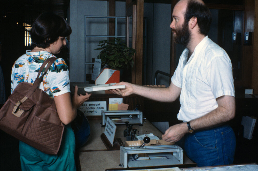 Slide 66 Library staff John Steers handing book to student