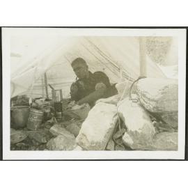 [Image of a man lying inside a tent, smoking a pipe.]