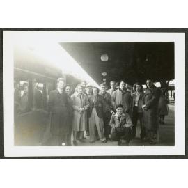 En Route [Image of a group of people standing at a train station, next to a train.]