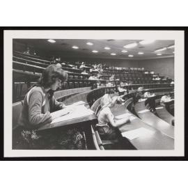 Students filling out forms in a lecture theatre (a)