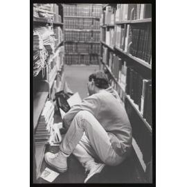 Student reading on the floor between library shelfs