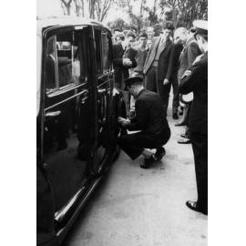 Governor General's chauffer removing coins from car hubcaps